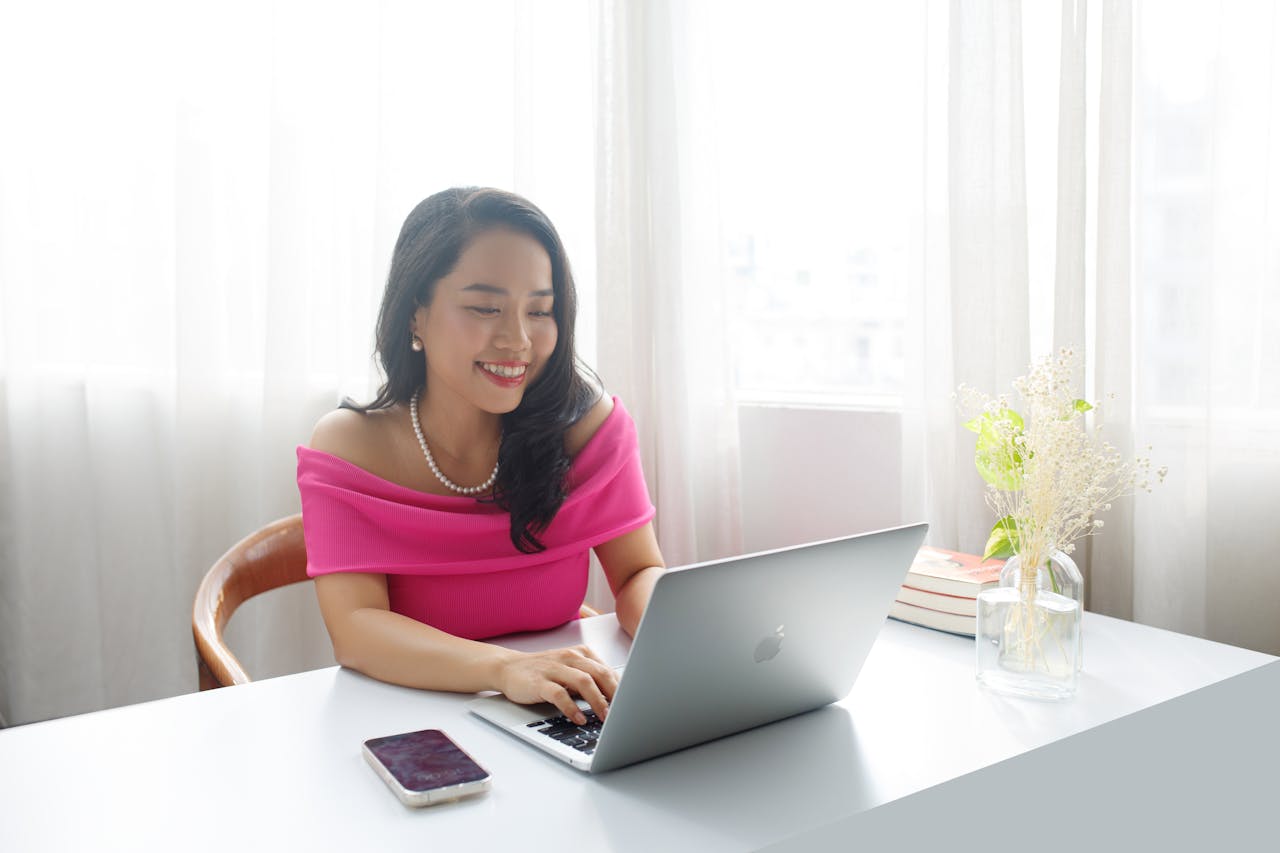 about-us Elegant businesswoman in pink dress working at a desk indoors, smiling and focused.