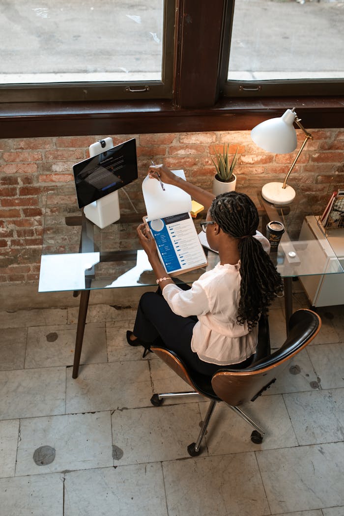 Overhead view of a woman at a glass desk working on a project in a stylish office.